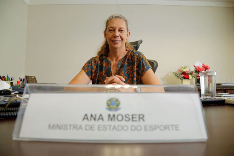 imagem de ana moser, ministra do esporte com uma placa com seu nome e cargo na frente